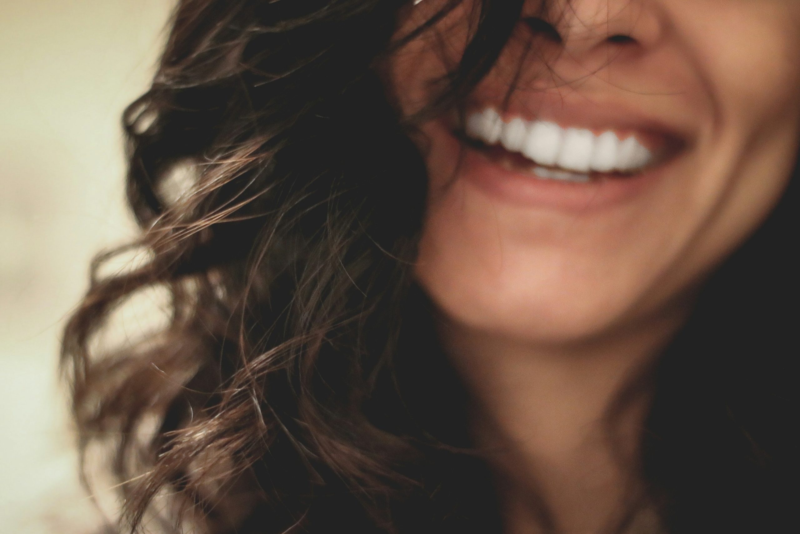 A woman smiling with her hair by the side of her face. Her smile is in focus.