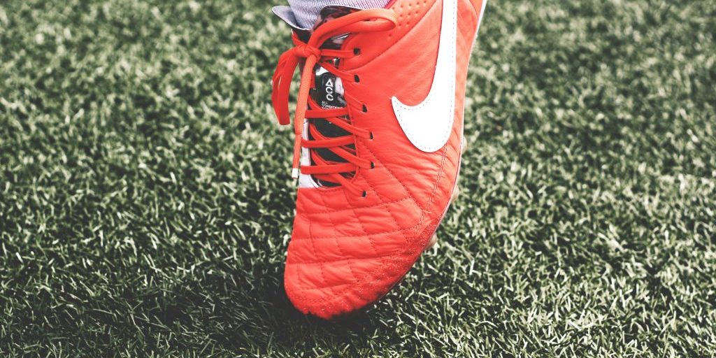 An orange football boot on grass